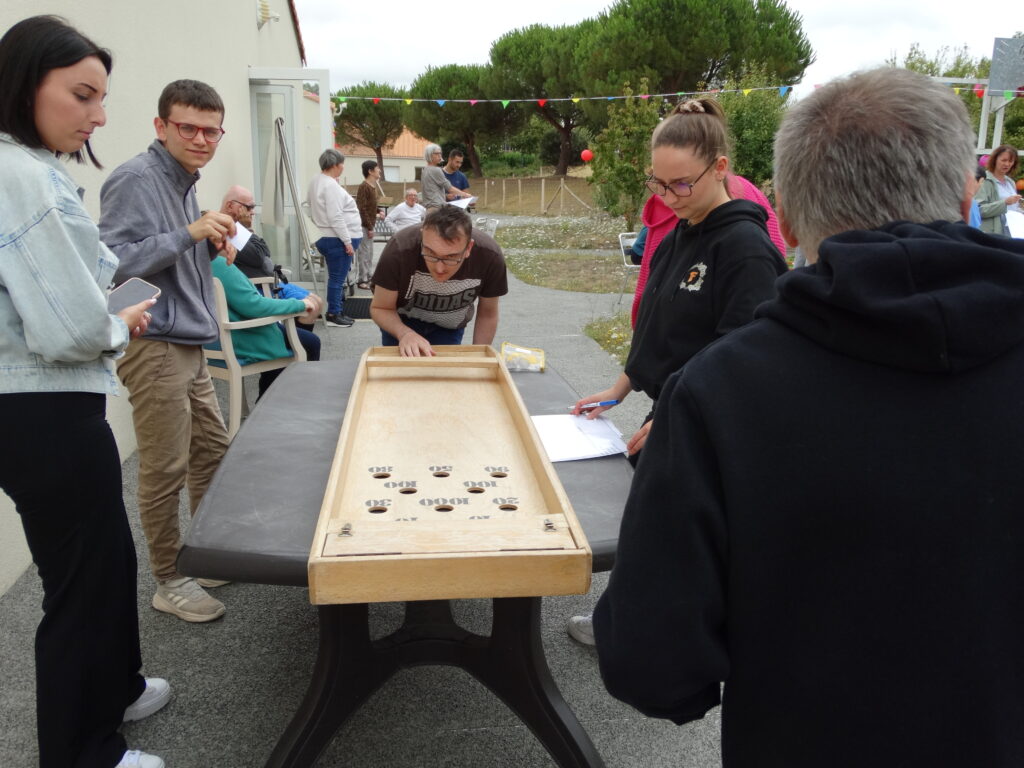 Les Résidents du centre d'habitat de d'aizenay jouent à des jeux en bois. Une jeune adulte joue à un jeu en bois où il doit faire glisser un palet dans un des trous de planche. Chaque trou correspond à un nombre de points.