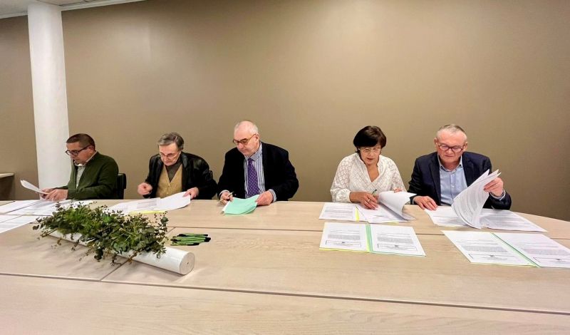 5 personnes sont assises de front et signent des documents